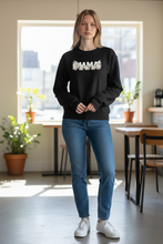 Load image into Gallery viewer, Woman wearing a black mama floral crewneck sweatshirt with neutral floral lettering, designed by SoJo Boutique, styled with jeans and white sneakers outdoors.
