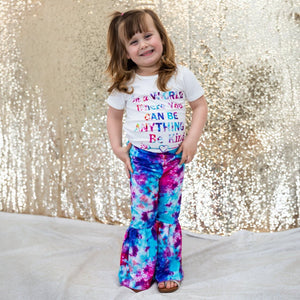 Tie dye bellbottom pants and tee shirt that says "in a world where you can be anything be kind"